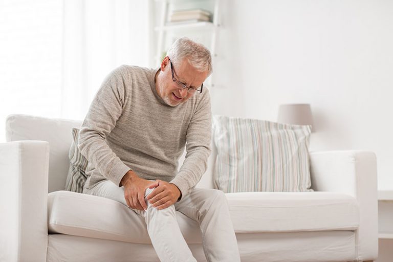 Man sitting on sofa holding knee in pain